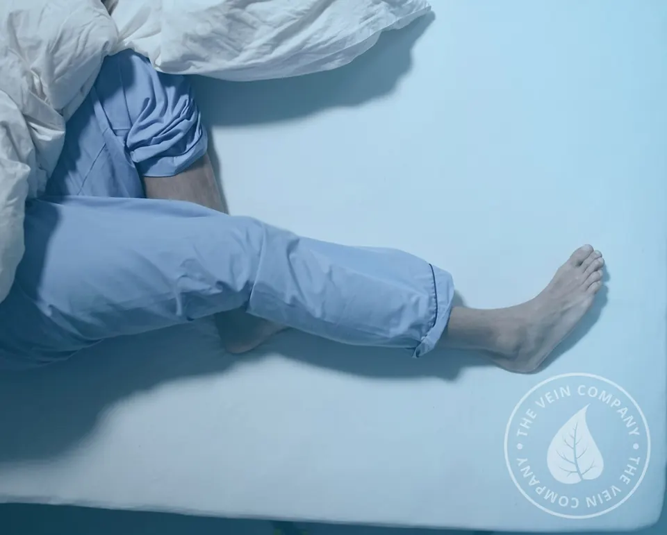 Person in bed at night rubbing their lower leg due to restless legs and nighttime cramps.